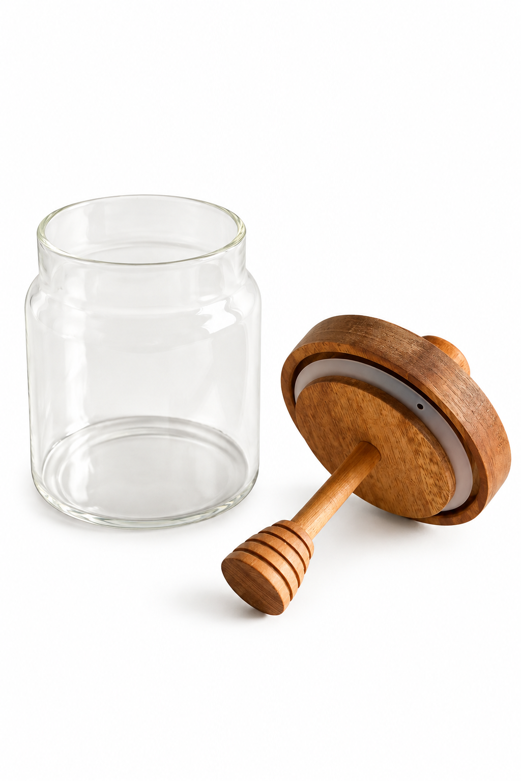 A clear glass jar with a wooden honey dipper lid resting beside it.