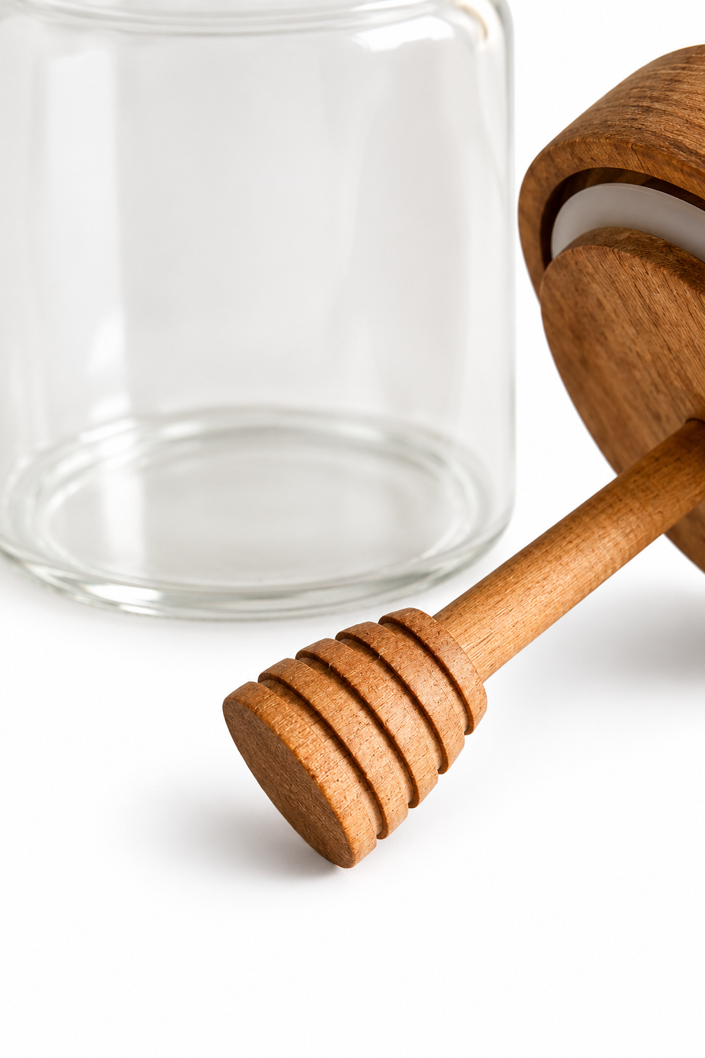 A close-up of a wooden honey dipper resting on a white surface next to a clear glass jar.